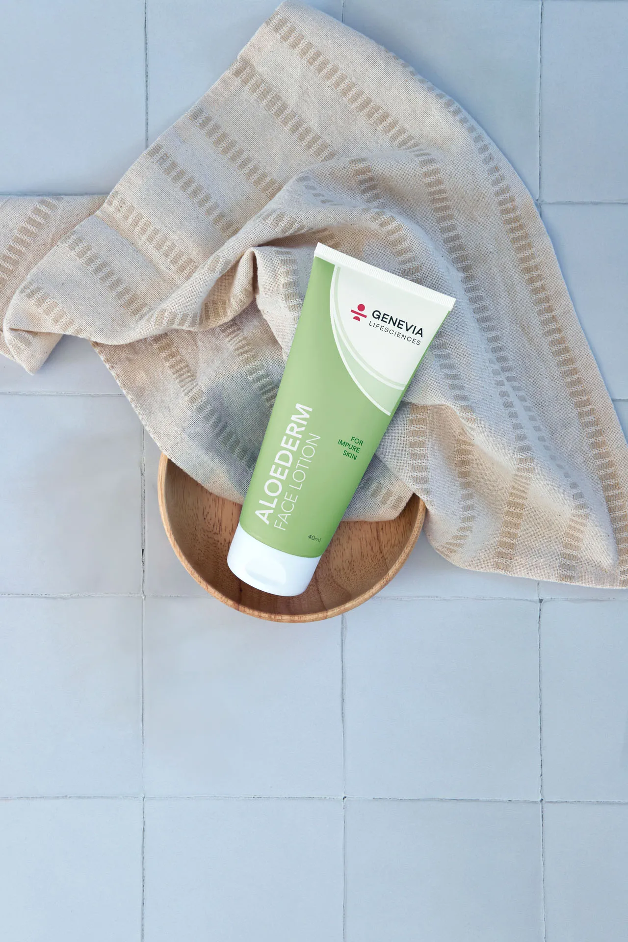 Aloederm Face Lotion i en træskål på et strikket tæppe mod lyseblå fliser