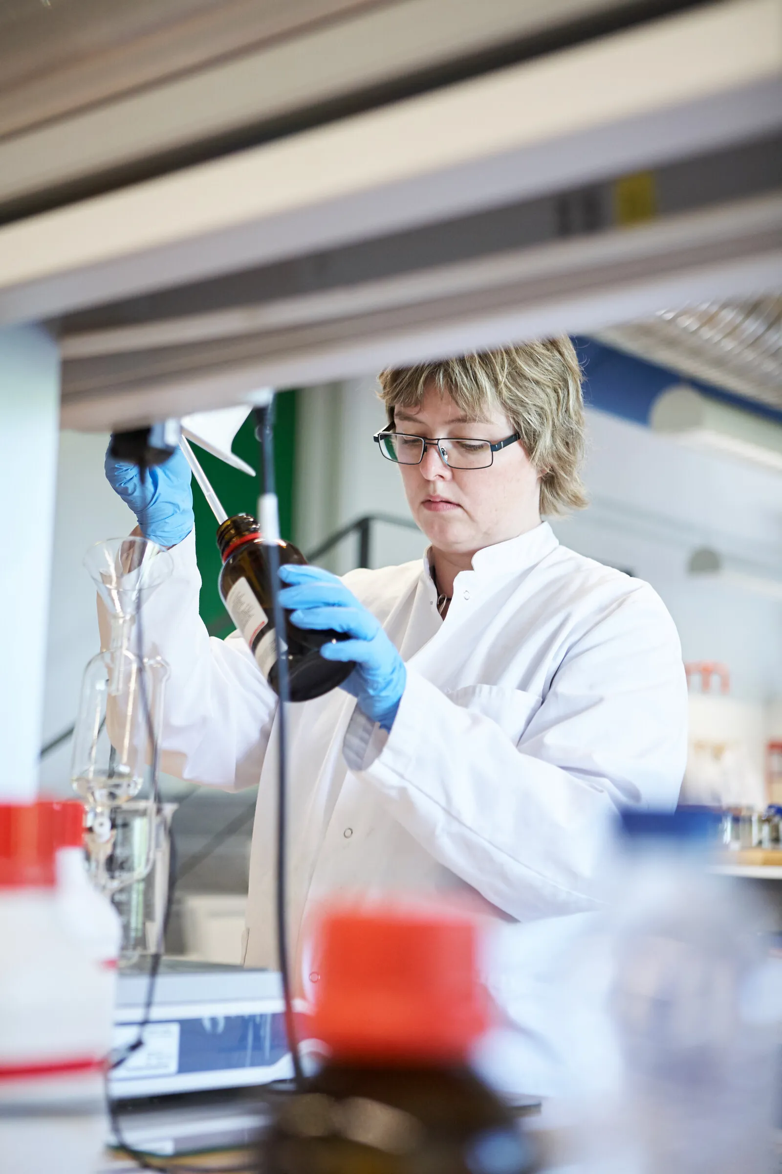 Laborant med handsker holder en flaske op i laboratoriet